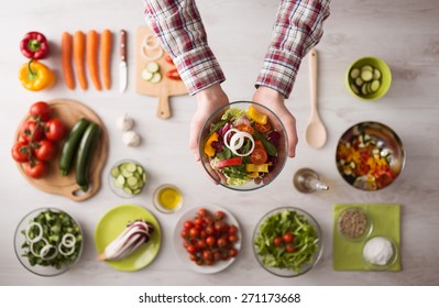 Man Holding A Fresh Garden Salad Bowl With Raw Sliced Vegetables, Hands Close Up Top View, Ingredients And Utensils On Background