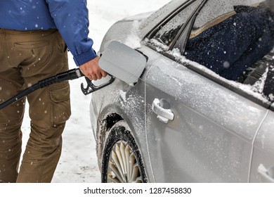 Man Holding Fuel Nozzle, Filling Gas Tank Of Car Covered With Snow In Winter