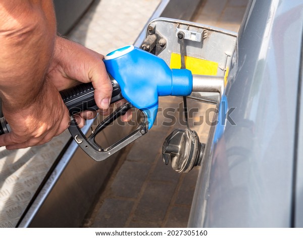 A man is holding a\
gas station pistol inserted into the fuel tank. A male fills the\
car\'s tank with fuel.