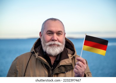 Man holding Germany flag. Portrait of older man with a national German flag. Visit Germany concept. Older man 50 55 60 years old with gray beard outdoors travelling. Travel to Germany Deutschland - Shutterstock ID 2232397467