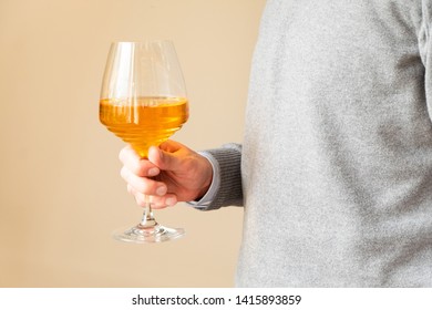 Man Holding A Glass Of Amber Wine On Neutral Background.