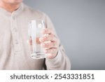 A man holding a glass of cold water with ice, showing a slight grimace due to tooth sensitivity. Image reflects the discomfort of consuming cold foods or drinks, highlighting dental health concerns