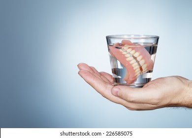 Man Holding A Glass Containing Old Dentures.