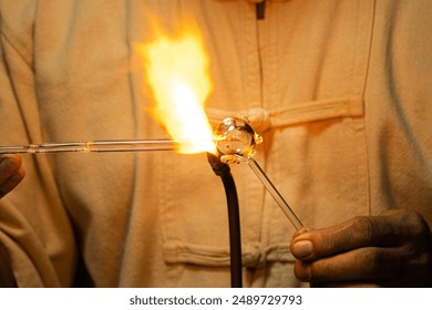 A man is holding a glass object that is glowing red hot. The man is wearing a white shirt and he is focused on his work. Concept of concentration and dedication to the task at hand - Powered by Shutterstock