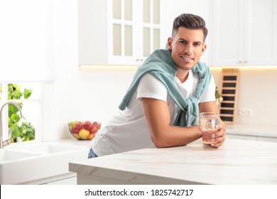 Man holding glass of pure water at table in kitchen