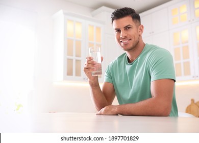 Man holding glass of pure water at table in kitchen. Space for text
