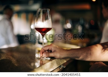 Man holding a glass of red wine in a restaurant or cafe on a wooden table in front of the window, romantic date, lunch break