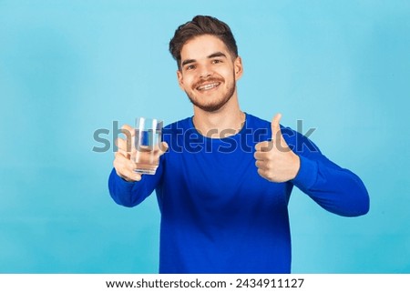 man holding a glass of water with one hand and with the other with the confidence up recommending drinking water and staying hydrated