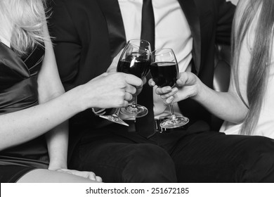 A man holding a glass of wine. Two girls standing in the background and drink wine. A man in a business suit and two pretty girls in the room. The concept of relationships between people.