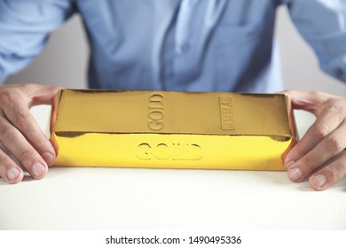 Man Holding Gold Bar On White Desk.