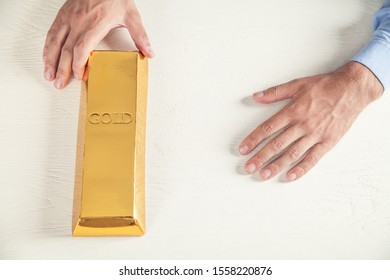 Man Holding Gold Bar On White Desk.