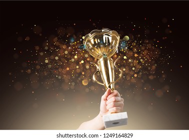 Man Holding Up A Gold Trophy Cup With Abstract Shiny Background, Copy Space For Text