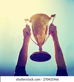 a man holding up a gold trophy cup as a winner in a competition toned with a retro vintage instagram filter effect app or action (backlit with the sun) - Shutterstock ID 270431966