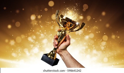 Man holding up a gold trophy cup with abstract shiny background, copy space for text