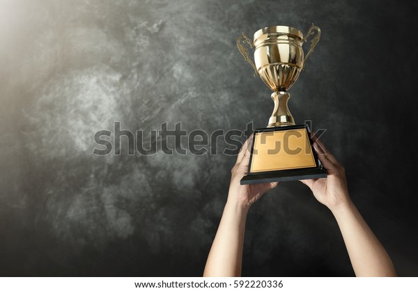 a man holding up a\
gold trophy cup with grunge wall background copy space ready for\
your trophy design.