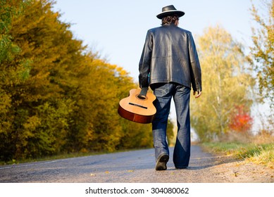 Man Holding Guitar And Walking Away On Country Road