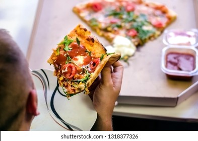 Man Holding Half-eaten Pizza Slice From The Box, Overhead Top View. Eating Alone. Italian Pastry With Tomato Sauce, Arugulla, Cheese And Ham. 