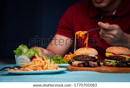Man holding hamburger on the wooden plate after delivery man delivers foods at home. Concept of binge eating disorder (BED) and Relaxing with Eating junk food. Stock fotó © 