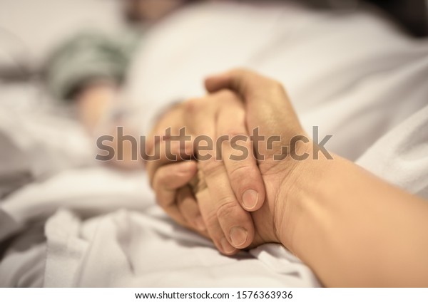 Man holding hand, giving support and
comfort to woman, loved one sick in hospital bed.
