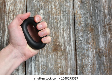 Man is holding in hand the hand grip strengthener. Expander on the wooden background. Sporty wrist builder for everyday trainings. - Powered by Shutterstock