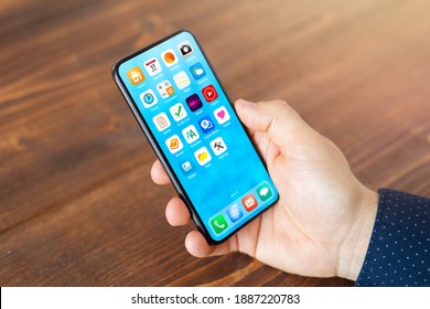 Man holding in hand mobile phone with different everyday application icons on home screen - Shutterstock ID 1887220783