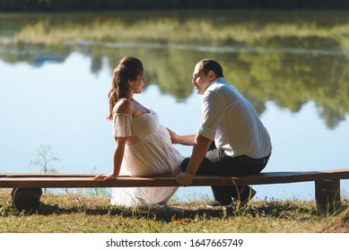 man holding hand on belly of pregnant woman on bench at river - Shutterstock ID 1647665749
