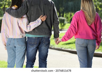 Man Holding Hands With Another Woman While Hugging His Girlfriend During Walk In Park, Back View. Love Triangle