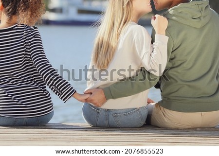 Man holding hands with another woman behind his girlfriend's back on pier near river, closeup. Love triangle
