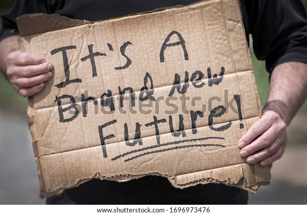 Man holding handwritten cardboard sign, It\'s a Brand New\
Future, coronavirus global pandemic, hope, change, pivot, adapt,\
job, employment, economy, uncertainty, positive thinking, win,\
victory, 