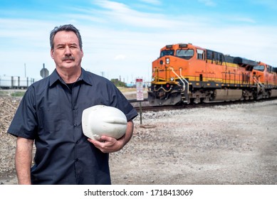 Man Holding Hard Hat Standing In Front Of Train Locomotive In Train Yard, Worker, Railroad, Rail Tracks, Transportation, Diesel Engineer, Conductor, Portrait