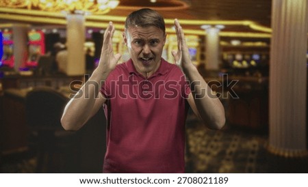 Man holding head with both hands in casino building, grimacing over lost bets at glowing slot machines; distress loss regret.