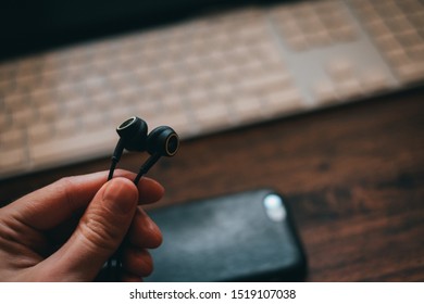 Man holding headphones with smartphone and keyboard in background - Shutterstock ID 1519107038