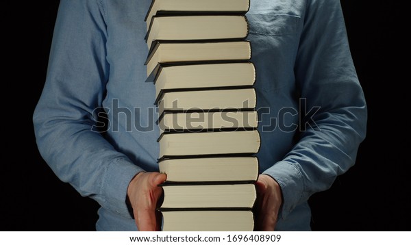 Man\
Holding A High Pile Of Thick Black Books In His\
Hands