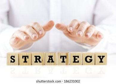 Man holding his hands protectively over the word Strategy on a row of wooden cubes in a conceptual image, closeup of the cubes and hands. - Shutterstock ID 186231002