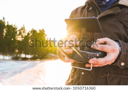 Man holding in his hands remote controller joystick transmitter flying the drone with sun shining bright day outdoors