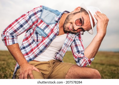 man holding his hat while sitting on a chair in a field outdoor
