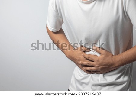 The man is holding his stomach with his hand against the white background, indicating that he has stomach pain.