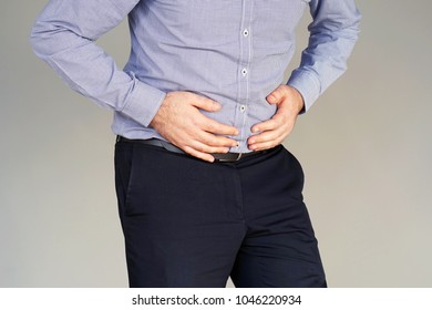 Man Holding His Stomach In Pain On Gray Background. Businessman Suffering From Abdominal Pain. Body And Health Care Concept.