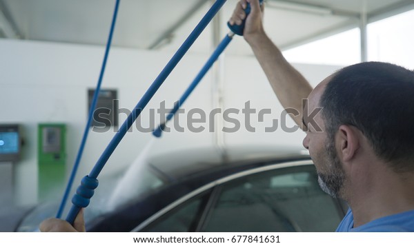 A man is holding a hose in a car washing machine and\
cleaning the car 
