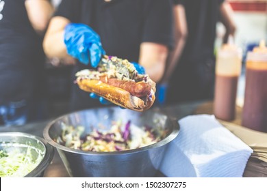 Man holding hot dog and adding vegetable salad. Street fast food vendor concept. - Powered by Shutterstock