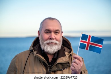 Man holding Iceland flag. 
Portrait of older man with a national Icelandic flag. 
Visit Iceland concept. Older man 50 55 60 years old 
with gray beard outdoors travelling in winter. Travel to Iceland