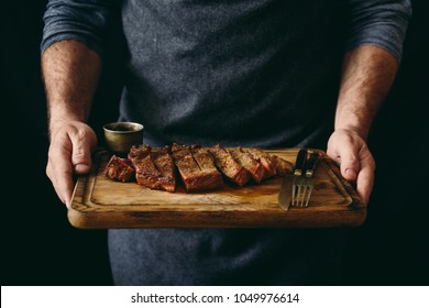 Man holding juicy grilled beef steak with spices on cutting board - Powered by Shutterstock