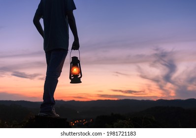 Hombre sostiene una lámpara de queroseno o una linterna en la cima de una montaña por la noche con el cielo justo después de la puesta del sol.