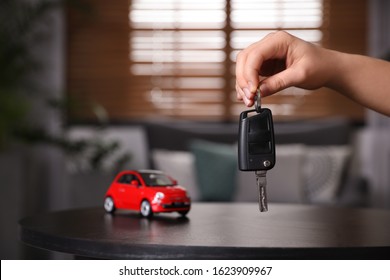 Man holding key near table with miniature automobile model indoors, closeup. Car buying