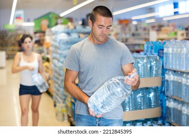 Man Holding Large Bottle Of Water, Making Purchases In Supermarket.