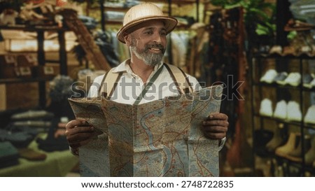 Man holding a large folded map and looking up in a building clothing shop, wearing pith helmet and backpack straps; curiosity travel exploration.