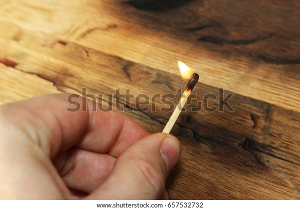 A man holding a lit match. This image also contains a\
wooden background and can be used to represent fire starting or\
arson. 