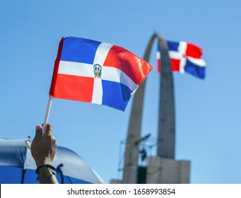 A Man Holding A Little Dominican Flag With The Flag Monument (plaza De La Bandera) In The Background