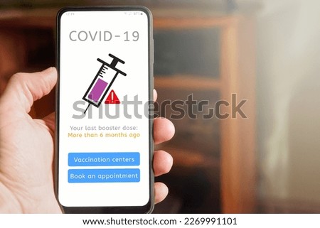 Man holding mobile phone with Covid-19 vaccine report, app interface saying that his last booster dose was more than 6 months ago, with buttons to see vaccination centers and to schedule appointment.