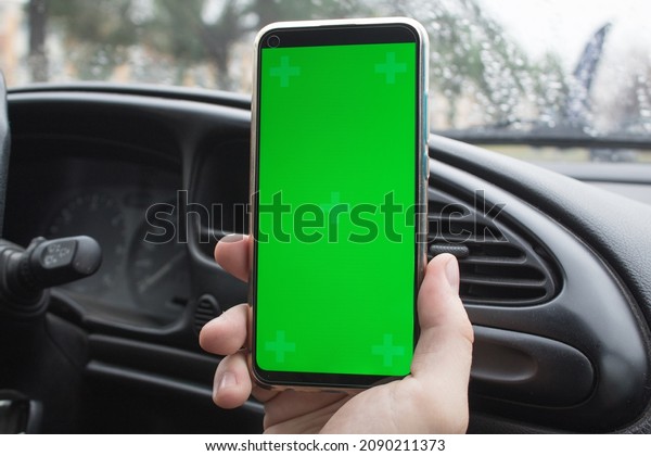 A man is holding a mobile phone, a smartphone\
against the background of the black interior of the car. Green\
screen, empty phone, app. swipe your thumb to the right. chromakey.\
online shopping